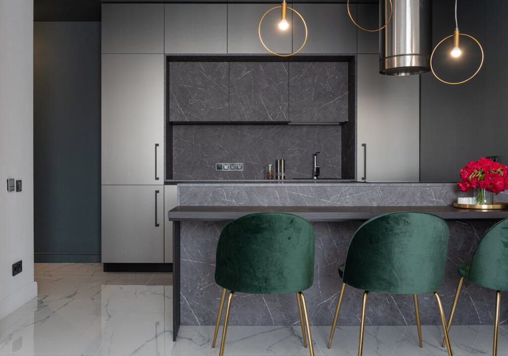 Interior of modern kitchen furnished with armchairs near counter decorated with vase of flowers and gray cupboards