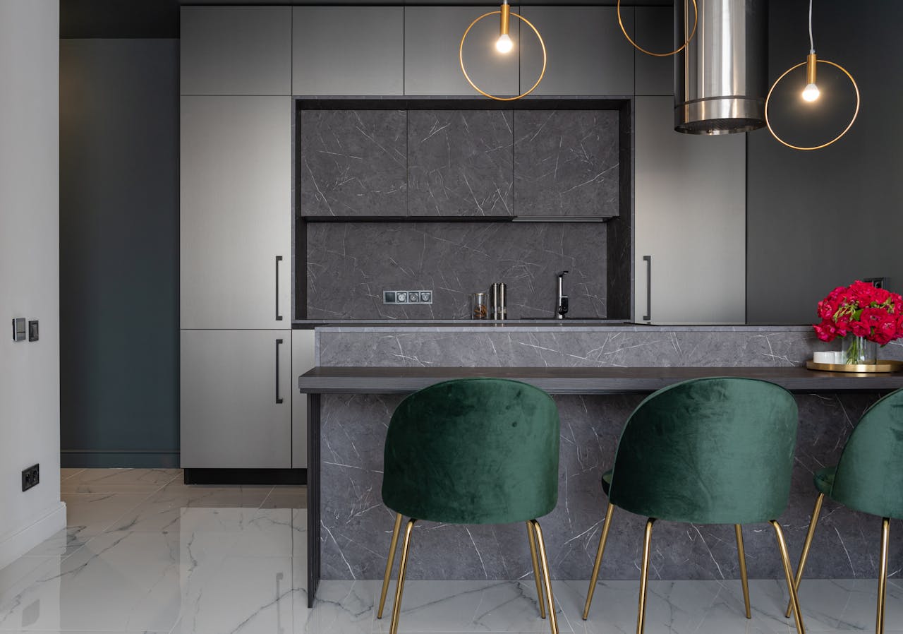 Interior of modern kitchen furnished with armchairs near counter decorated with vase of flowers and gray cupboards